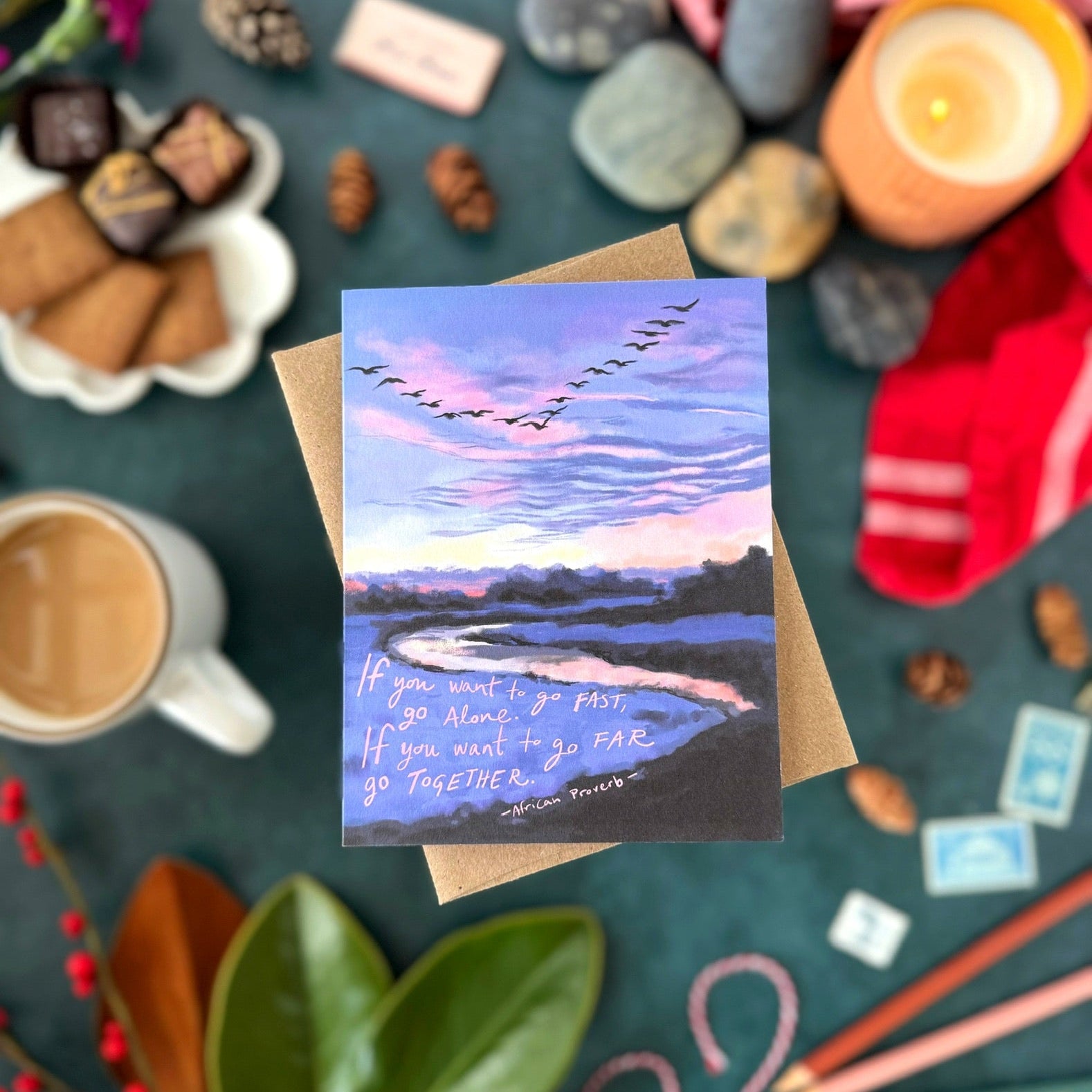 Greeting card that says, "If you want to go fast, go alone. If you want to go far go together," with scenic design on a table with coffee, snacks, and candles.