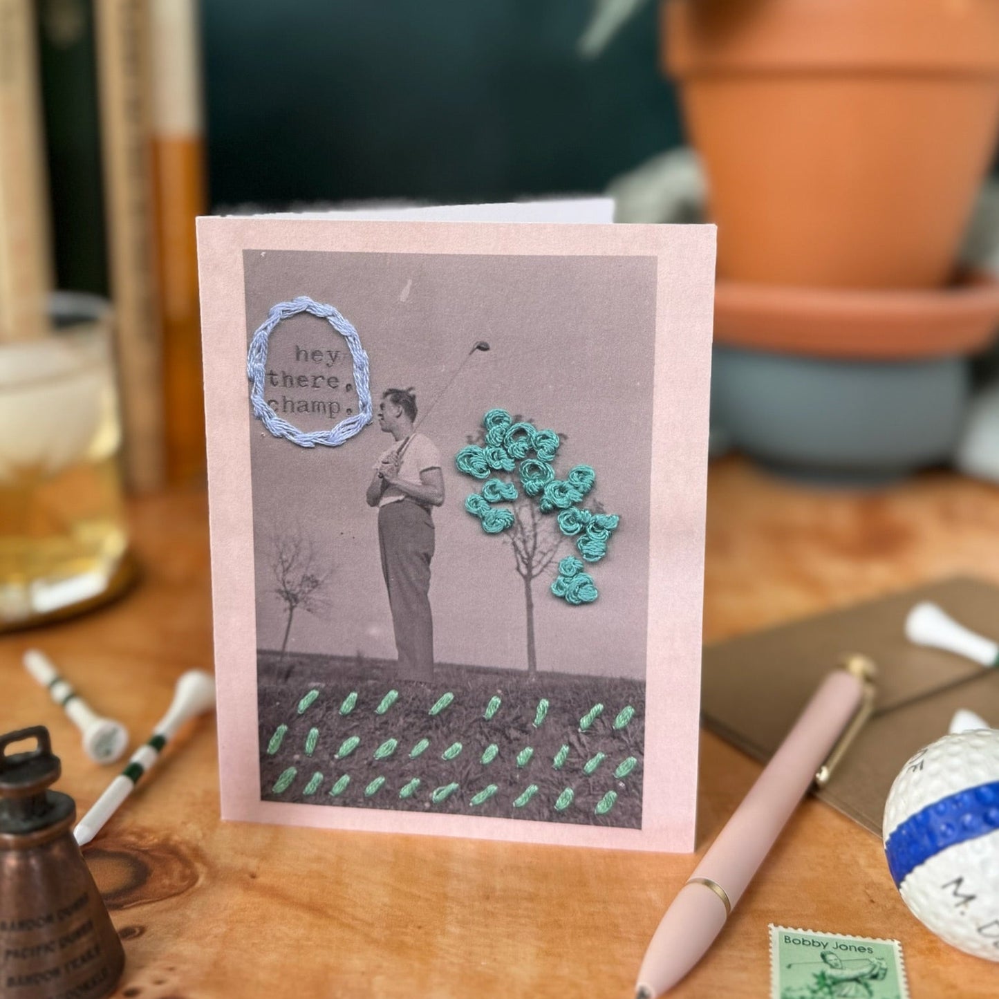 Greeting card with a design of a person holding a golf club next to a tree on a wooden surface.