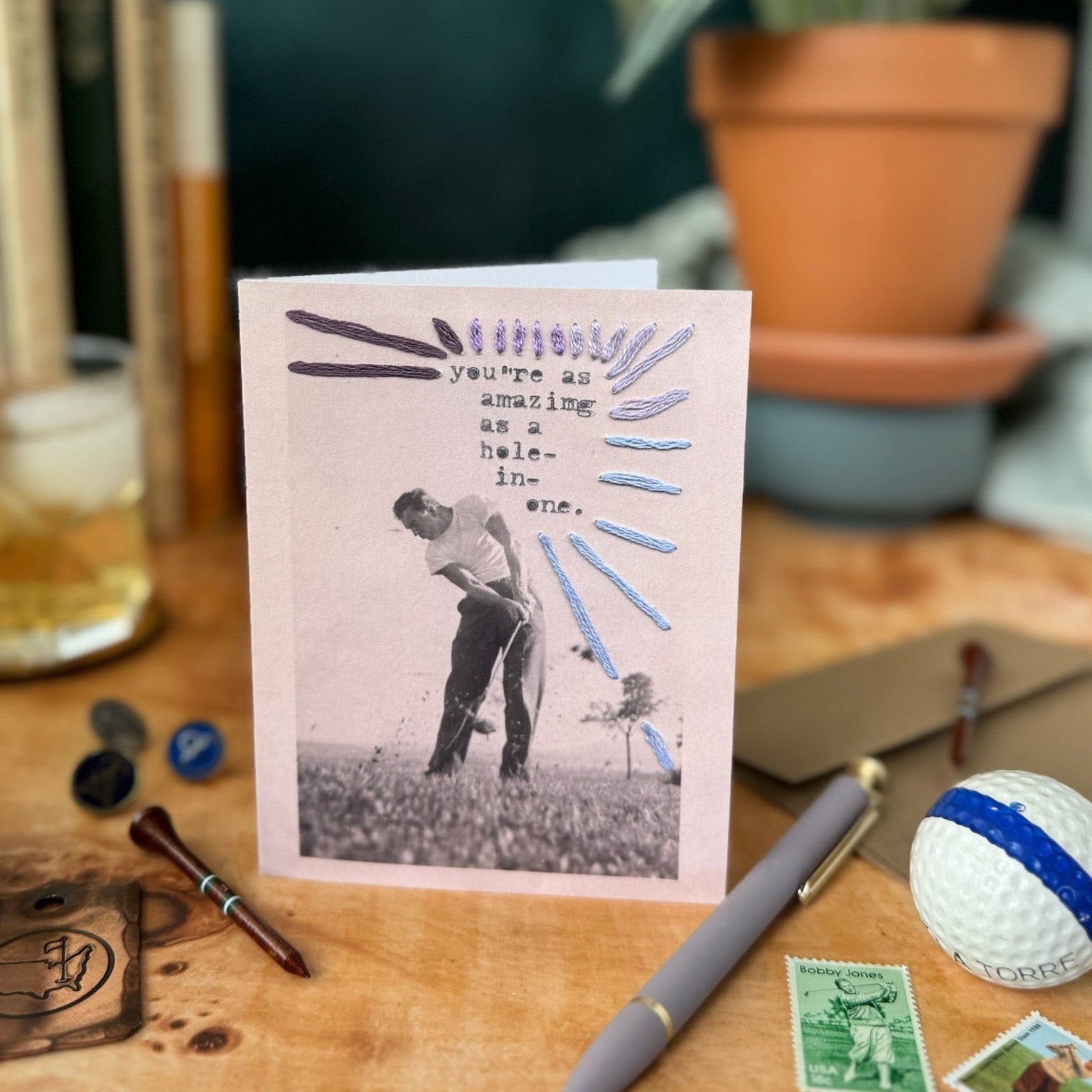 Greeting card with a golf-themed design on a desk with stationery items.