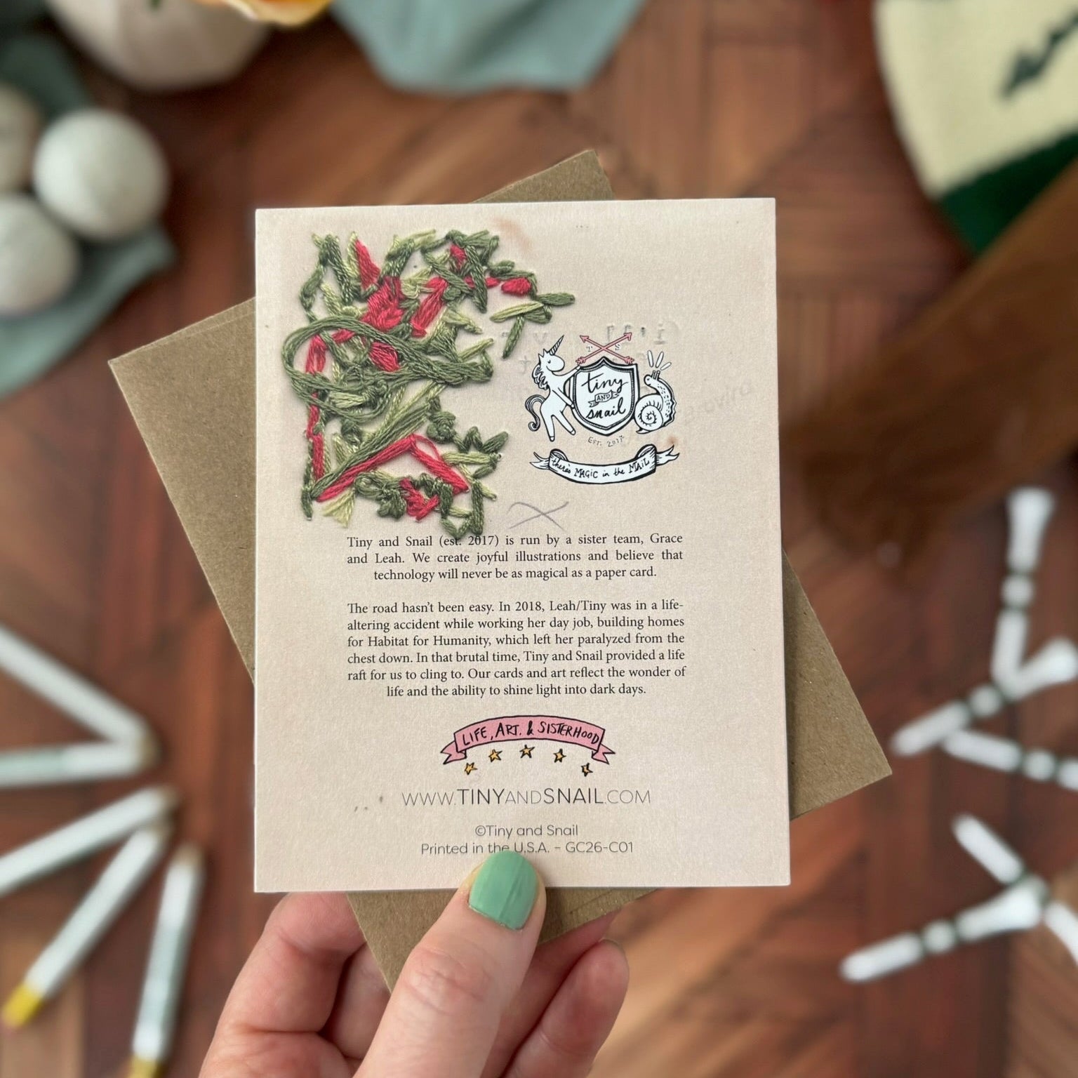 Hand holding a card with decorative elements on a wooden surface