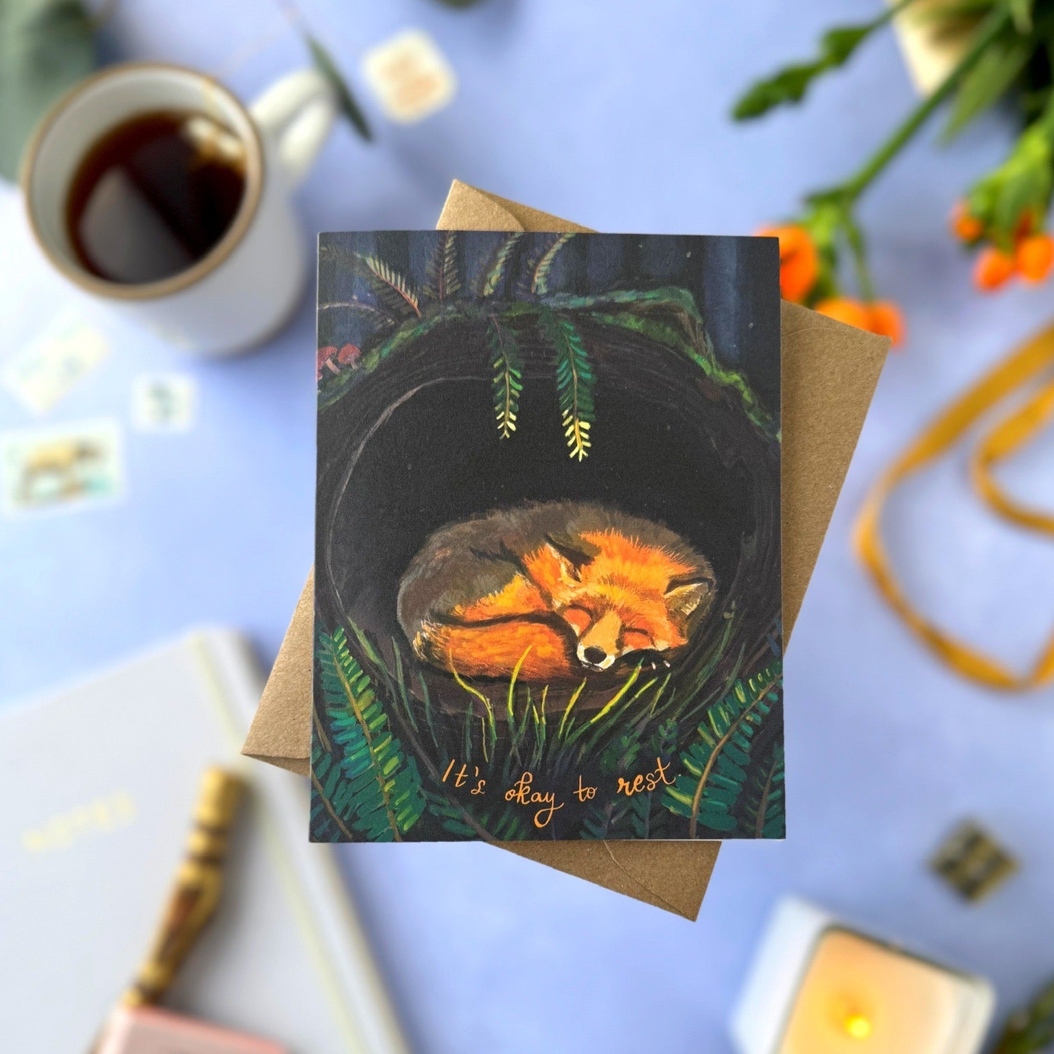 Greeting card with fox illustration on a blue surface with coffee and candles.