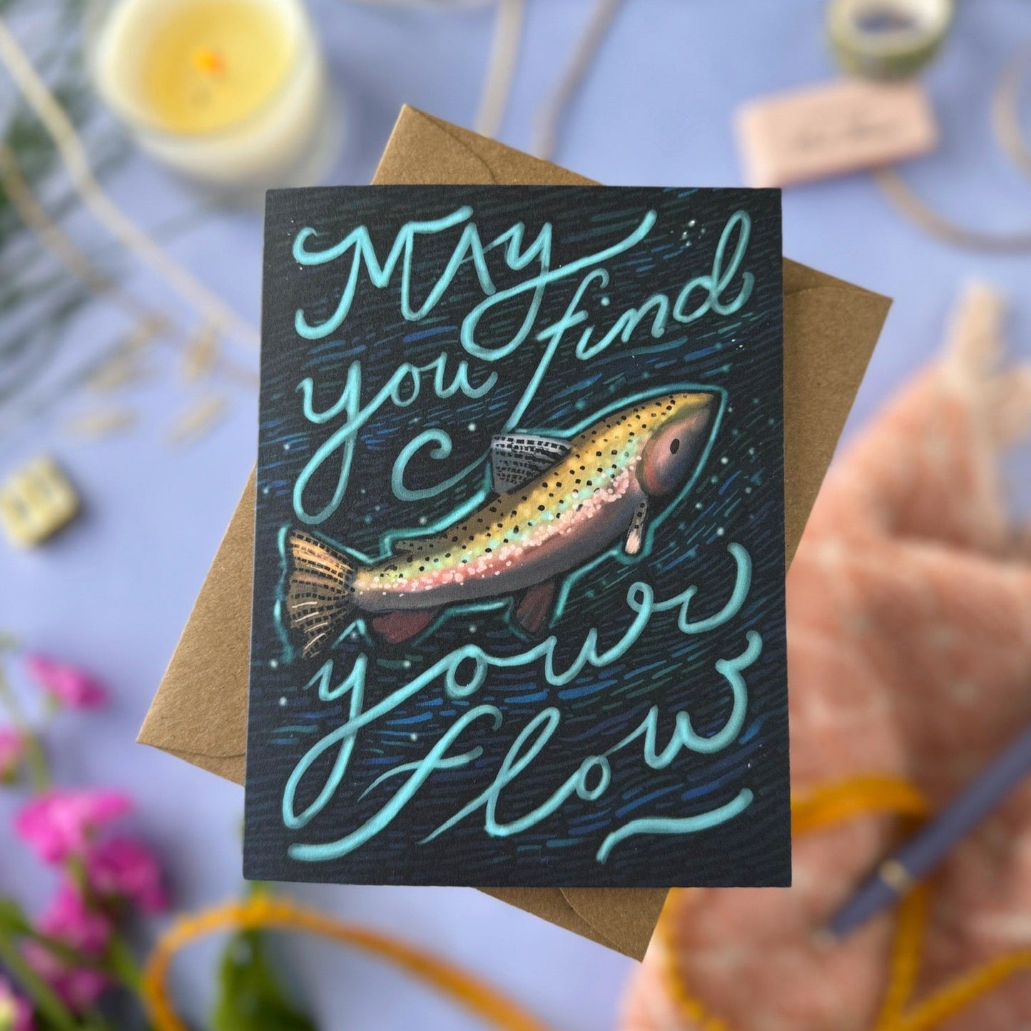 Greeting card with fish illustration and text 'May you find your flow' on a blurred background.