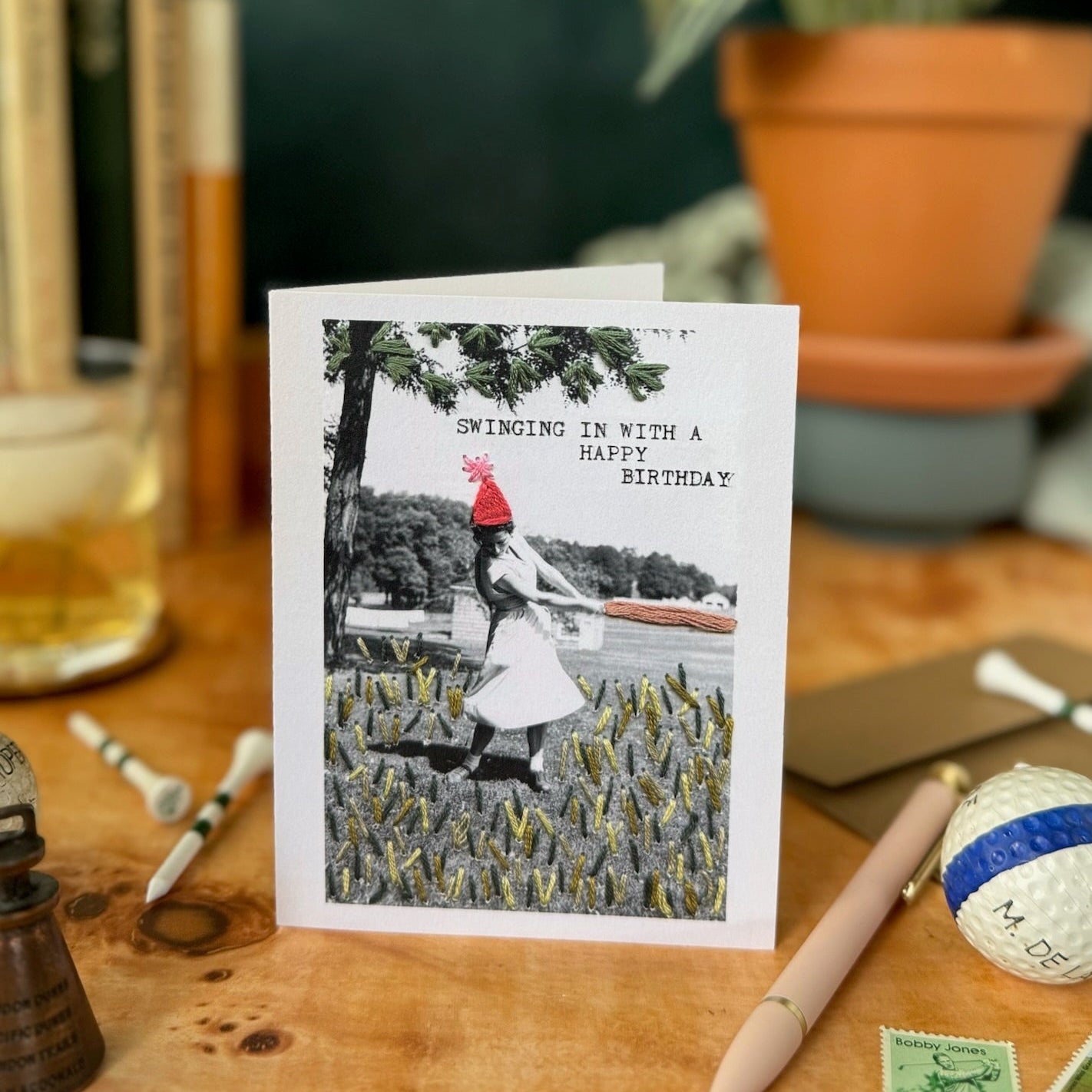 Greeting card with black and white photo of a woman in a field, placed on a wooden surface with stationery items.