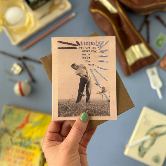Hand holding a vintage-style card with a person in a field, surrounded by stationery items on a blue background.