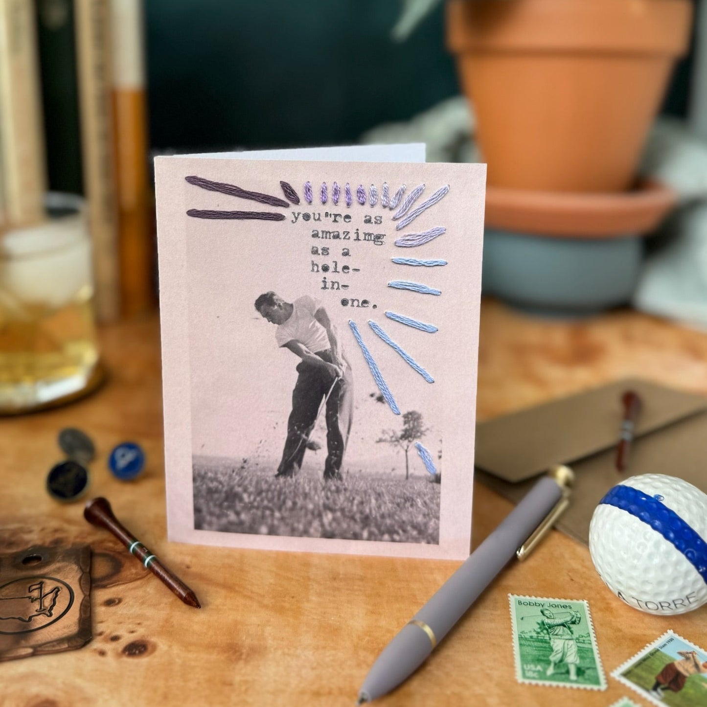 Greeting card with a golf-themed design on a desk with stationery items.